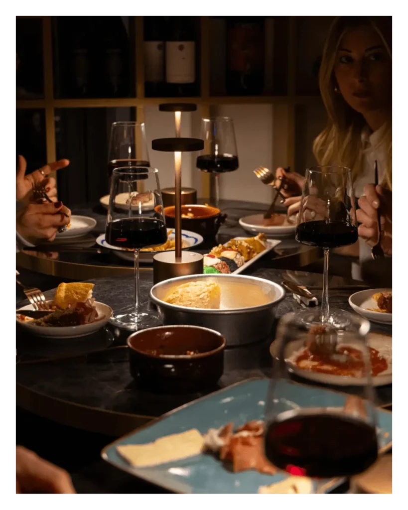 Tavola imbandita per una cena siciliana gourmet da Talé Milano Isola con calici di vino rosso, polpette al sugo e piatti della tradizione in un'atmosfera intima con luci soffuse.